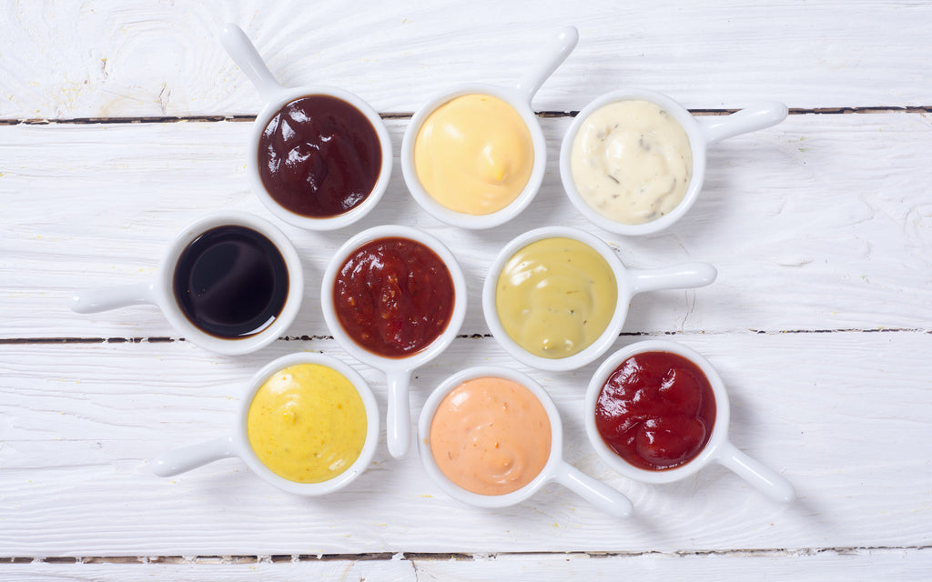 Variety of sauces in small porcelain bowls on a white wooden surface