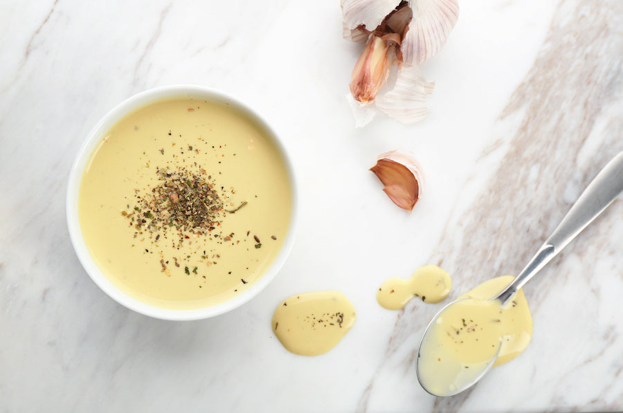 Vegan mayonnaise in a white bowl with garlic and stainless spoon