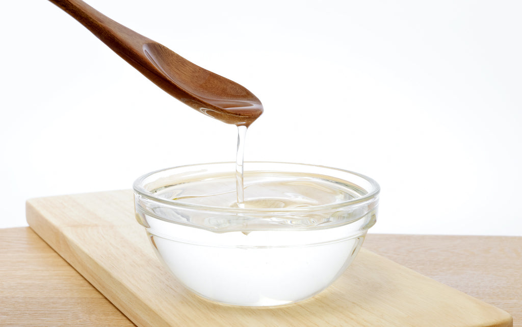 C8 MCT oil: Oil dripping from a wooden spoon into a glass bowl on top of a wooden board