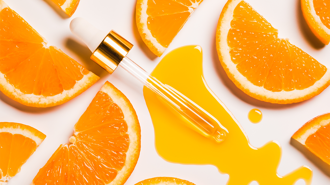 A pipette expels an orange liquid on a white backdrop, surrounded by orange segments