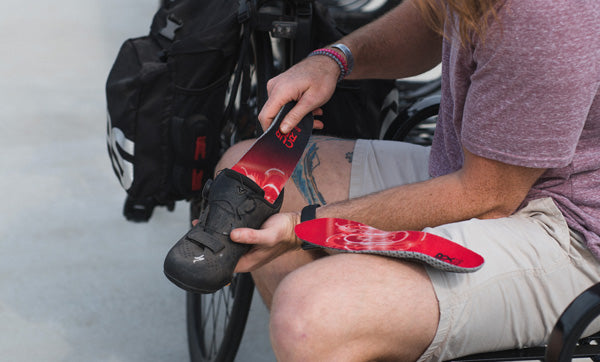 man sitting on bench placing red low profile insole into cycling shoe