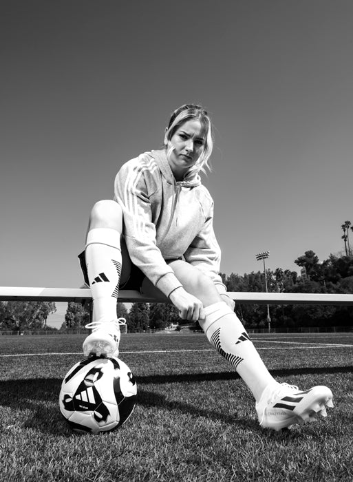 CURREX Ambassador Lindsey Horan sitting on bench in soccer field with soccer ball under foot