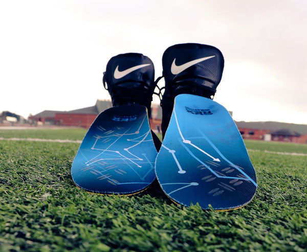 Blue insoles for cleats and a pair of football cleats on a field