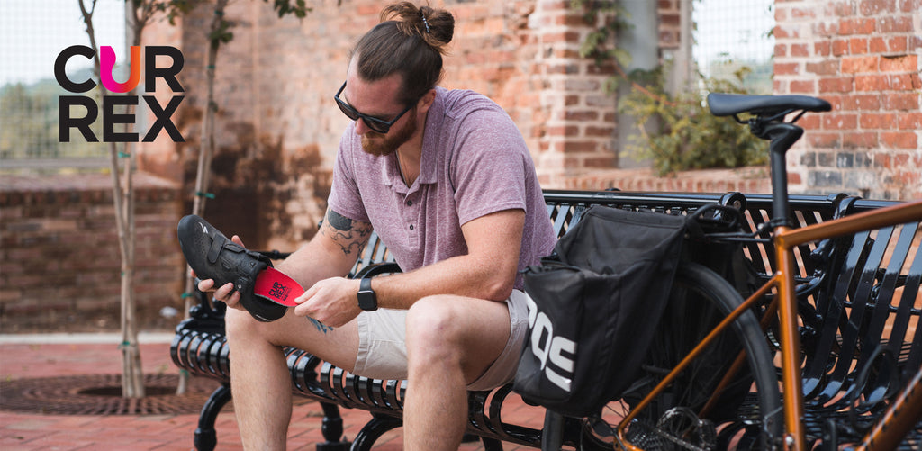 Man sitting on outdoor bench and placing red cycling insole into cycling shoe