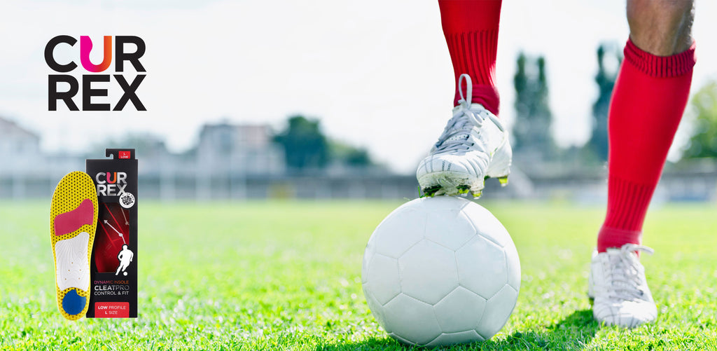 Person wearing cleats on soccer field standing with one foot on soccer ball