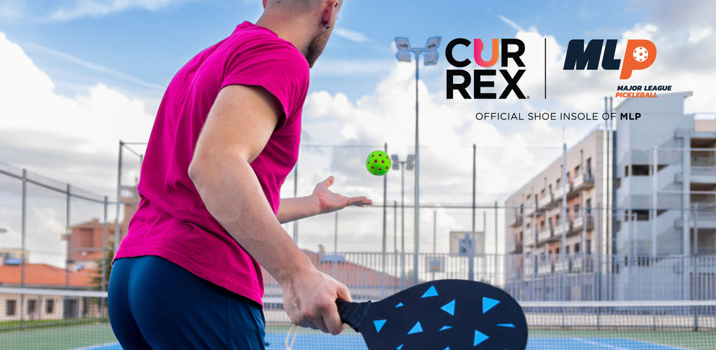 behind a young man tossing a pickleball into the air for a serve