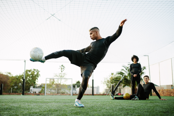 Man kicking soccer ball with teammates in background