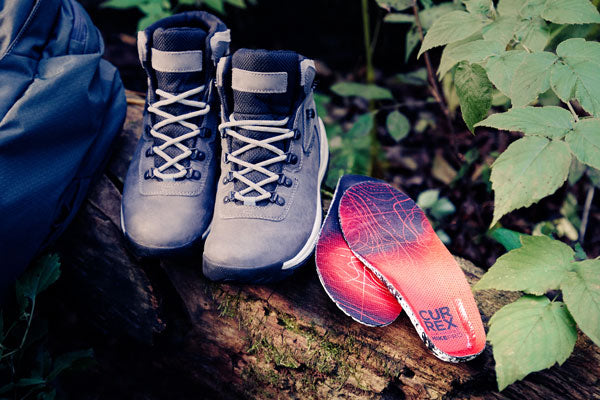 Pair of hiking boots next to red insoles for hiking boots outside