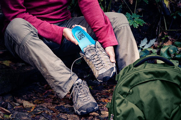 Person placing blue hiking insole into hiking shoe while outside