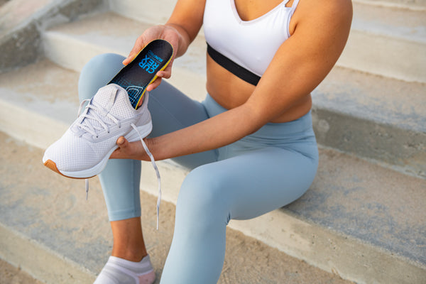 woman sitting on steps and placing running insole into grey running shoe