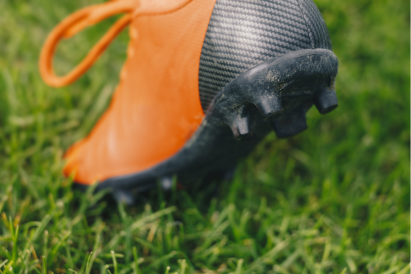 Orange and black soccer cleat on grass