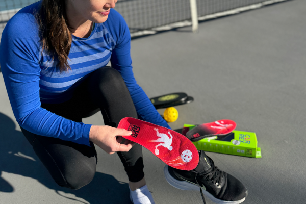 woman kneeling on pickleball court while placing pickleball insole into black shoe