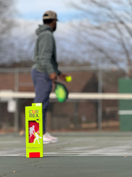 box of pickleball insoles with man playing on pickleball court in the background