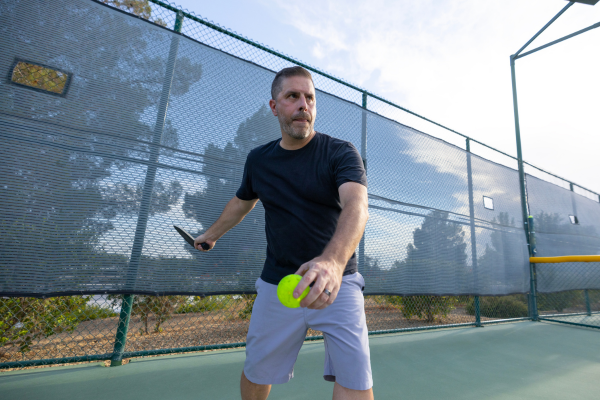 man serving a pickleball with arm and paddle swung behind him