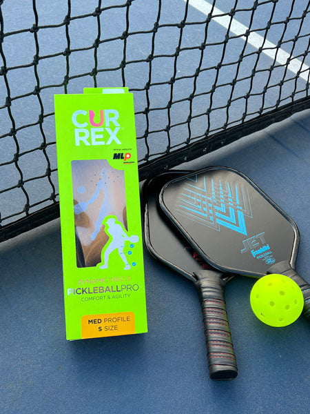 boxed pickleball insoles on a pickleball court with pickleball paddles and ball
