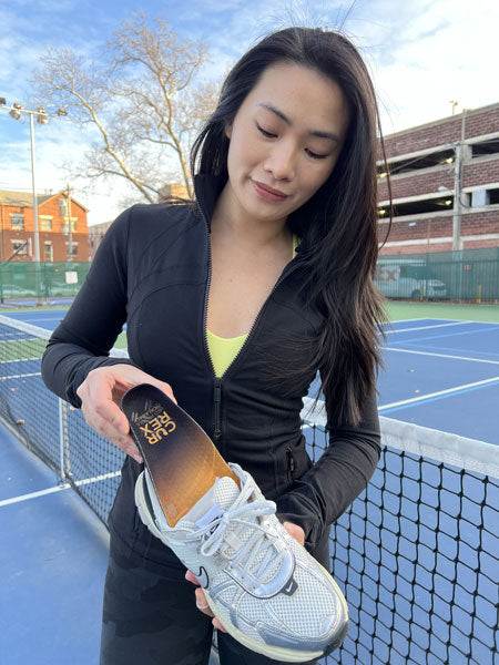 woman placing a pickleball insole into a white shoe on an outdoor court