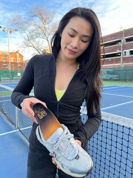 woman on pickleball court placing yellow insole into white shoe