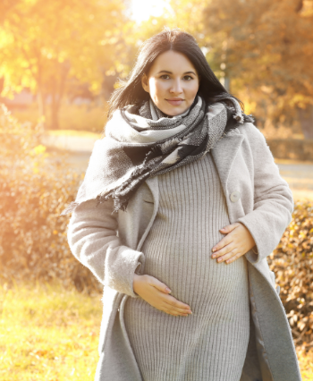 stylish pregnant woman wearing a long coat with overlay rib-knit dress and scarf in autumn