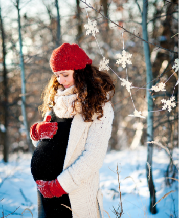 pregnant woman holding her belly standing outside in the snow