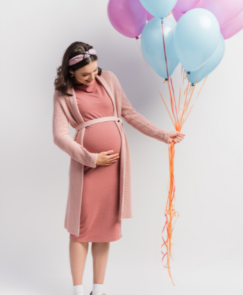 pregnant woman holding balloons in hand and smiling at her baby bump