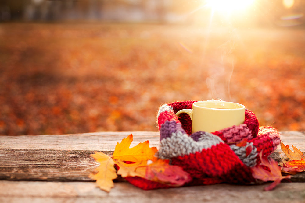 A cup of tea wrapped in a woolen scarf on an autumn day next to yellow leaves