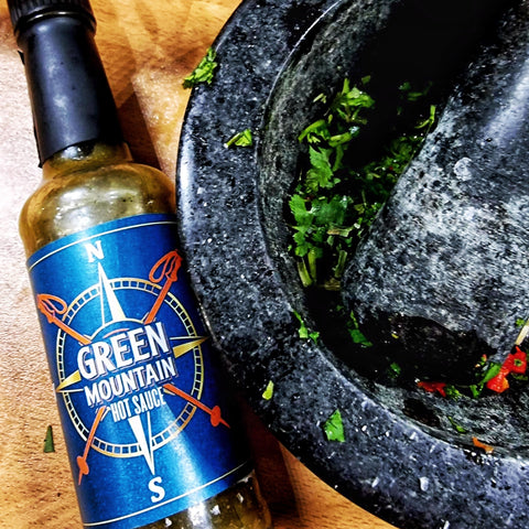 Green Mountain Hot sauce laid next to a pestle and mortar filled with Chimichurri