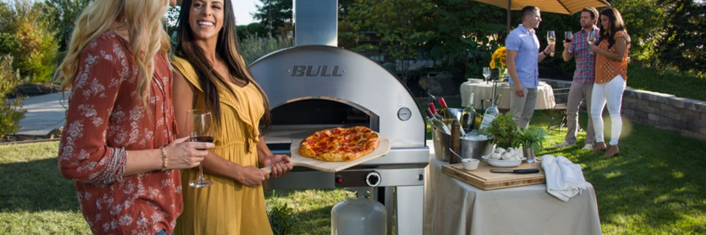 People standing around a Bull Pizza Oven at back yard