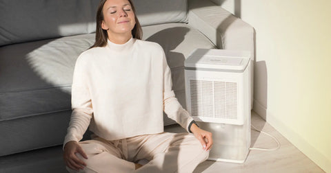 A woman seated in meditation by a portable dehumidifier, illustrating a calm and clean air environment that can contribute to better sleep quality through optimal humidity levels.