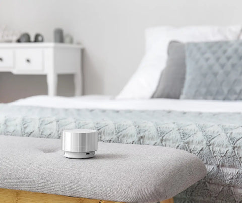 A compact white noise machine on a bedside bench, ready to provide sound masking for a restful night in a well-organized bedroom.