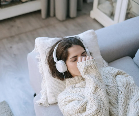 A woman relaxes on a couch wearing headphones, a peaceful expression on her face as she listens to white noise to unwind.