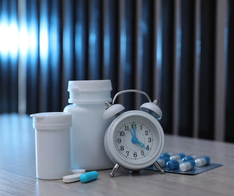A bedside table showcasing a bottle of melatonin tablets, a white alarm clock, and several pills laid out in front.