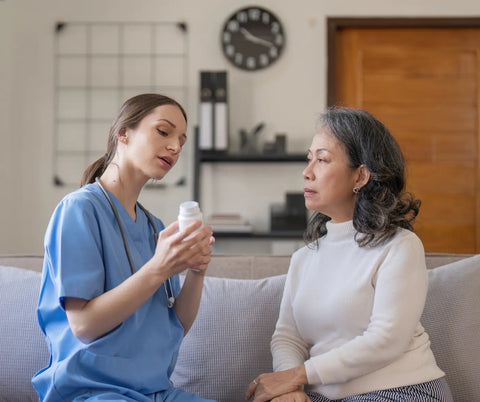 A healthcare professional discusses a bottle of melatonin supplements with an attentive older adult woman in a living room.