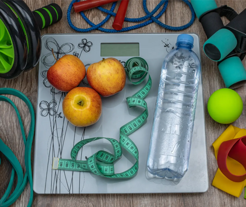 A balanced array of fitness equipment and healthy food options, including apples, a water bottle, and a measuring tape on a scale, representing alternatives to stress eating for a healthier lifestyle.