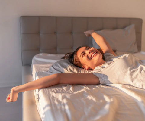 A joyful awakening after a refreshing sleep, with arms stretched wide in a sunlit, serene bedroom, suggesting the benefits of sound masking for sleep quality.