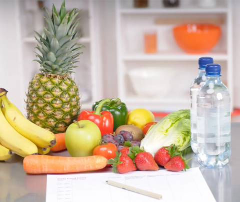 A variety of fresh fruits and vegetables arranged neatly on a kitchen counter next to a bottle of water and a food diary, suggesting a planned approach to healthy eating as a strategy to combat stress eating.