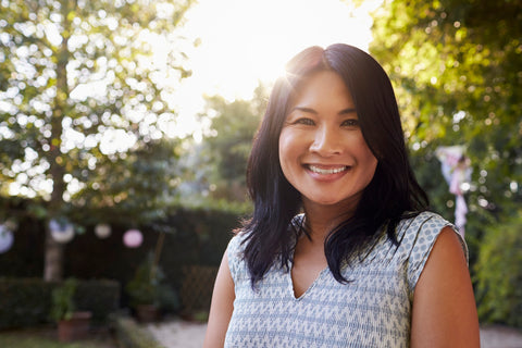 Woman smiling with sun and trees behind her