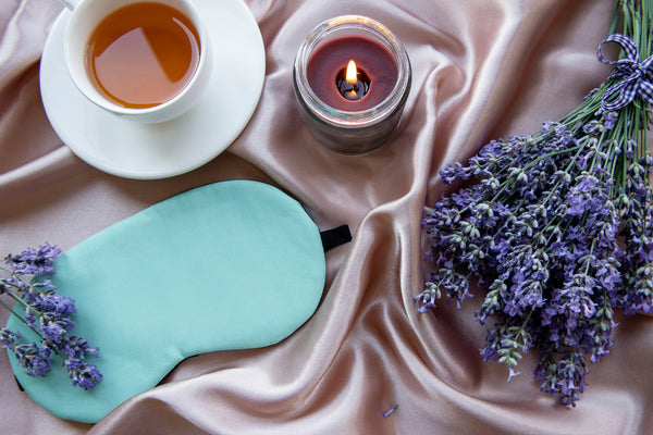 An eye mask, lavender oil, green tea, and a lit candle.