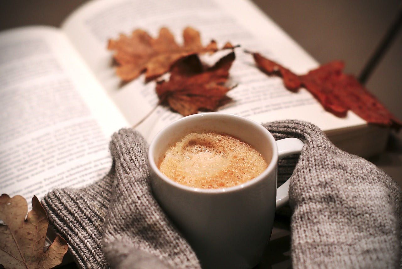 Sweater-covered hands holding coffee in front of open book