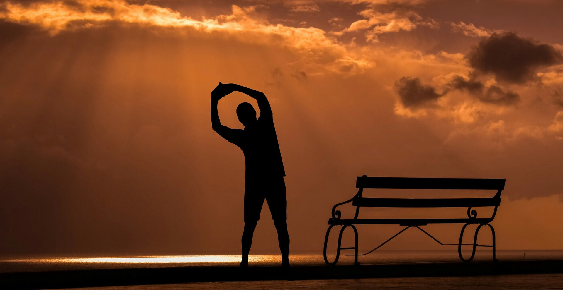 Person stretching near bench at sunrise or sunset