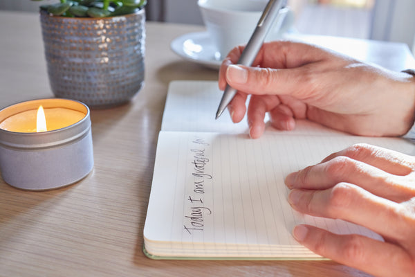 Journal and a Person Holding Pen on a Wooden Table.