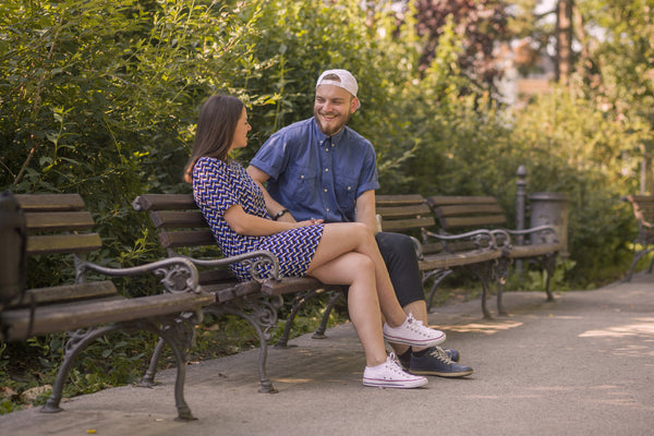 A happy couple sitting on a park bench, talking and smiling at each other.