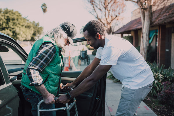 A person helping an elderly get out of a car.