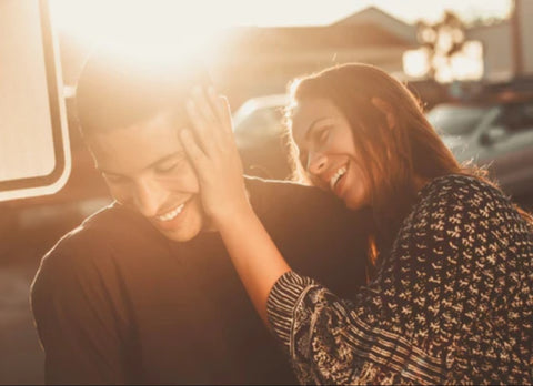 young man and woman playfully laughing with sun shining in the background