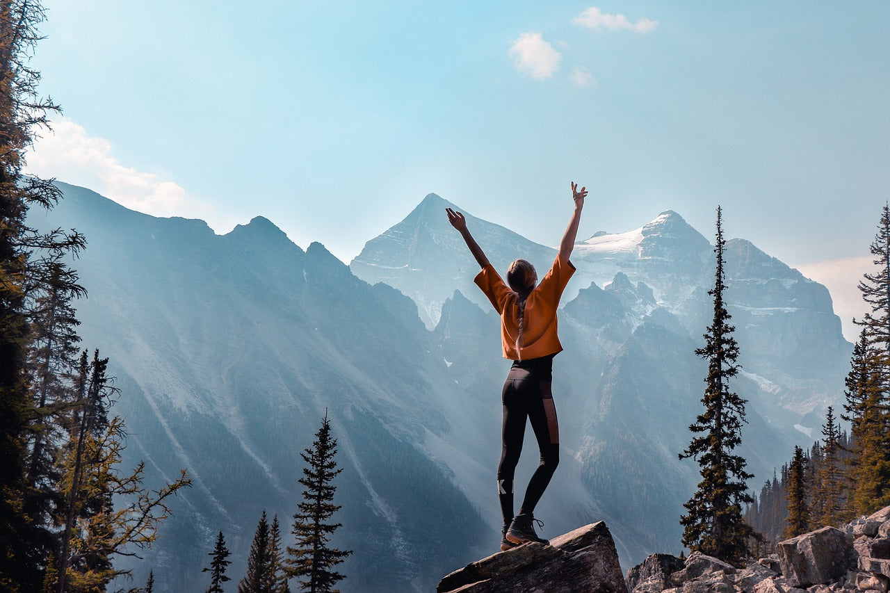 Person standing with arms up in front of mountains