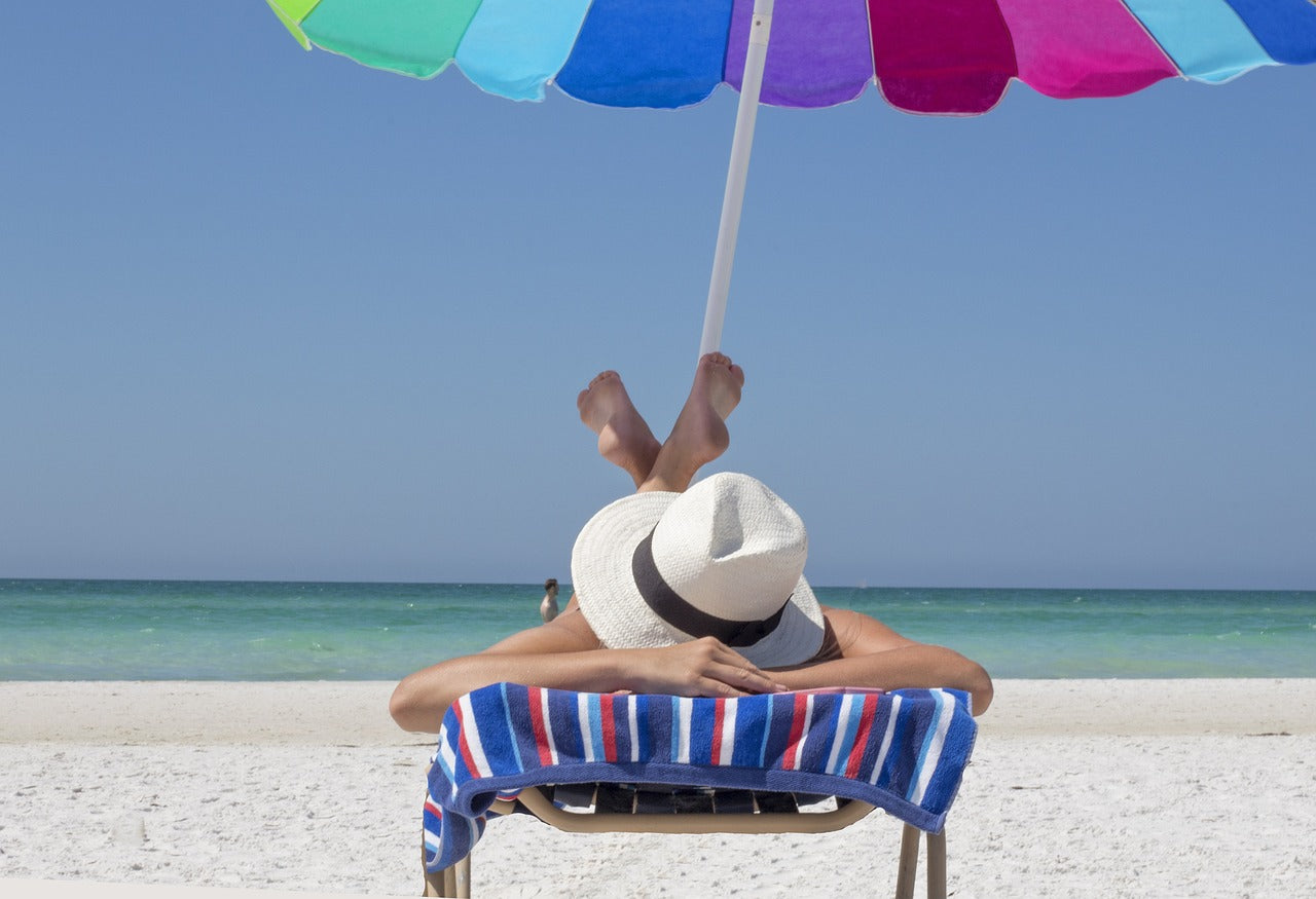Person laying under beach umbrella wearing a hat