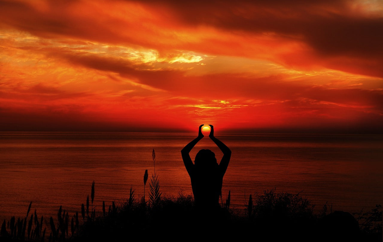 Person with hands around the sun in front of sunset