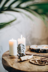 Une ambiance zen ! sur une table en bois est disposé 2 bougies parfumées, un encensoir et une statuette d'un dieux indien éléphant