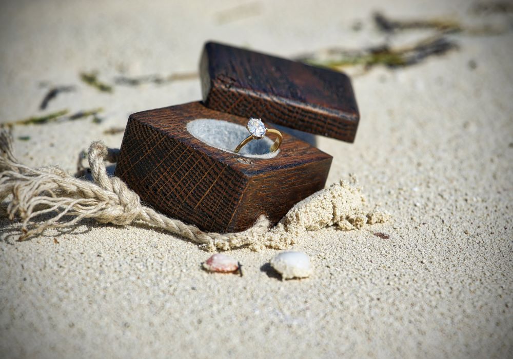 Un écrin en bois posé sur une plage renferme une bague sertie d'un diamant