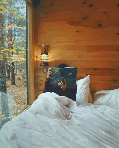 Une personne lisant un livre dans son lit qui aurez bien besoin d'un porte livre en bois metalz bien besoin d'un