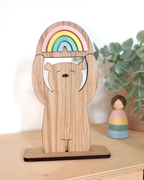 Wooden bear on a stand, holding a pastel coloured rainbow above his head